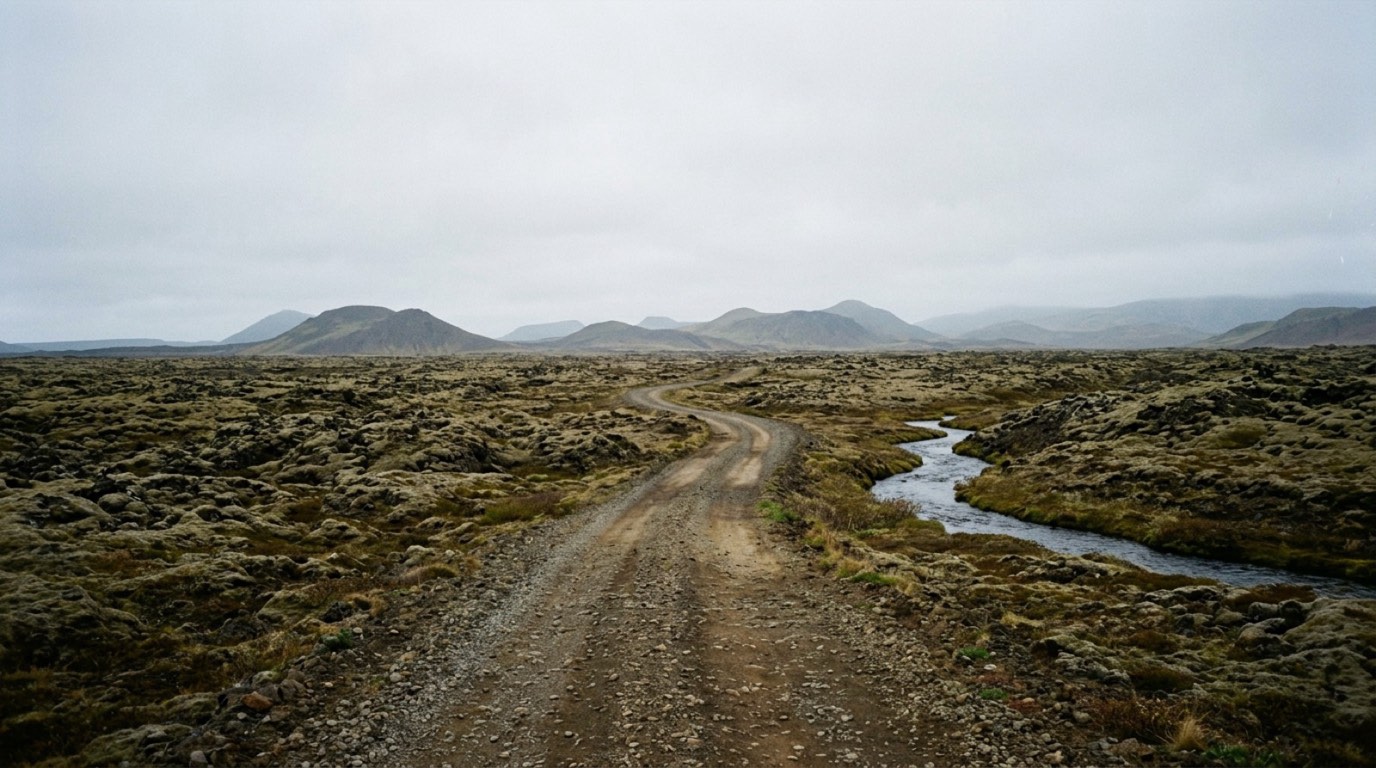 An open volcanic upland with a gravel track running through moss covered lava and low hills fading into mist, with no buildings and no people